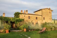 an old stone house with a lawn chair in the foreground and some plants around it