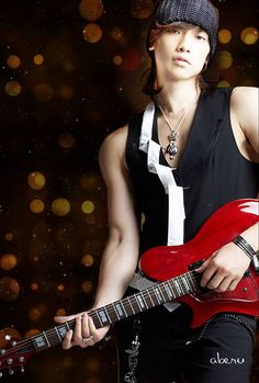 a woman holding a red guitar in front of a dark background with boke lights