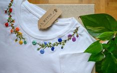 a white t - shirt with colorful flowers on it and a plant next to it