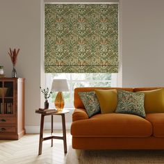 an orange couch in front of a window with roman shades