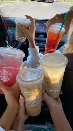 four people holding up starbucks cups in the back seat of a car with their hands on them