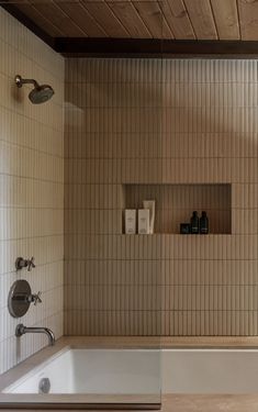 a bath tub sitting under a window next to a wooden ceiling in a room with white tile walls