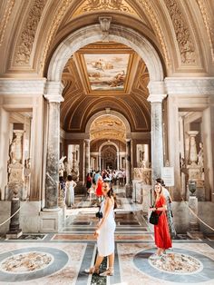 two women are standing in the middle of a hall with statues and paintings on the walls