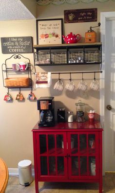 a red cabinet with cups on it in front of a door and coffee mugs hanging from the wall