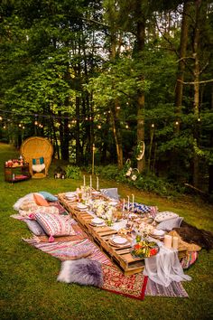 an outdoor dinner table set up in the middle of a forest with lights strung overhead