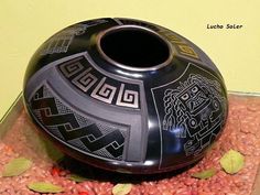 a large black vase sitting on top of a pile of red rocks next to a yellow wall