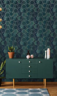 a green cabinet with some plants and candles on it in front of a patterned wall