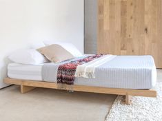 a bed with white sheets and pillows in a room next to a wooden headboard