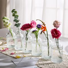 there are many vases with different flowers in them on the tableclothed table