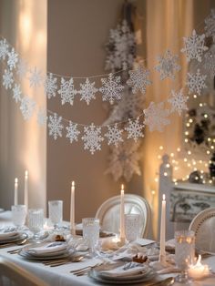 a dining room table set for christmas with candles and snowflakes hanging from the ceiling