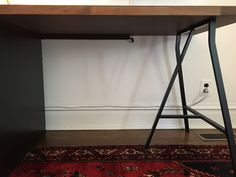 a wooden desk with metal legs and a red rug on the floor next to it