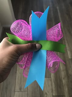 a hand holding a pink and blue bow on top of a wooden floor next to a wall