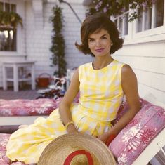 a woman in a yellow dress sitting on a bed with a large straw hat next to her