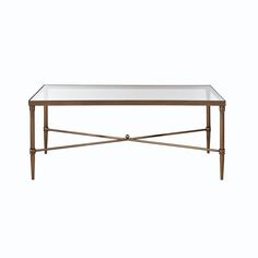 a glass table with metal legs and a gold frame around the top, against a white background