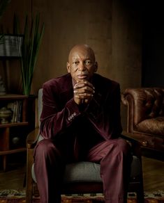 a man sitting in a chair with his hands clasped to his chest and looking at the camera