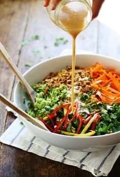 someone pouring dressing into a salad in a bowl