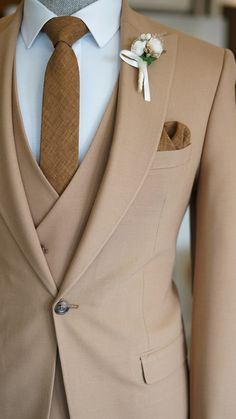 a tan suit with a brown tie and white flower boutonniere on the lapel