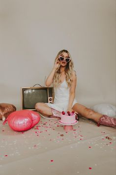 a woman sitting on the floor in front of a tv with balloons and confetti