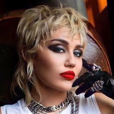 a woman with short blonde hair wearing black gloves and red lipstick is posing for the camera