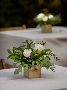 white flowers are in a wooden vase sitting on a table with greenery and candlesticks