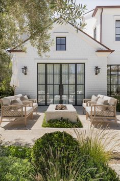 an outdoor living area with couches and tables in front of a white brick house