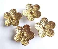 four gold flower shaped objects on a white surface