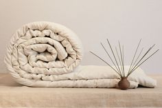 a white blanket sitting on top of a bed next to a plant