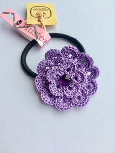 a purple crocheted flower on a black headband with a pink tag attached to it