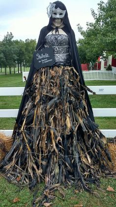 a scarecrow with a sign on it's head in front of a white fence