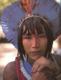 a native american woman wearing a blue headdress and holding her hand on her chest