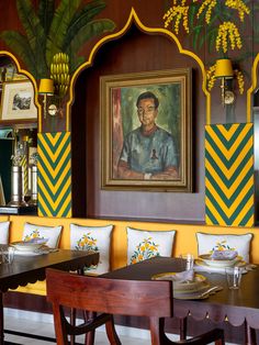 a dining room with yellow and green striped walls, wooden benches and artwork on the wall