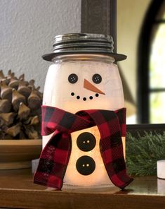 a lighted snowman jar sitting on top of a table next to a pine cone