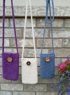 three crocheted purses hanging on a brick wall with flowers in the foreground