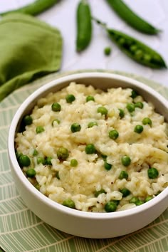 a white bowl filled with rice and peas on top of a green place mat next to asparagus