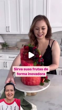 a woman standing in front of a cake with fruit on it