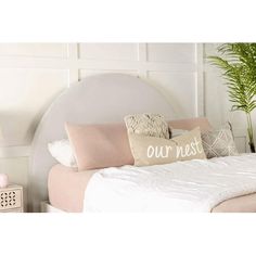 a white bed topped with lots of pillows next to a potted green plant on top of a wooden table