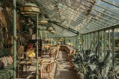 the inside of a greenhouse filled with lots of green plants and wicker furniture,