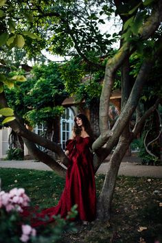 a woman in a red dress standing next to a tree