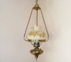 an old fashioned lamp hanging from a chain in a room with white walls and yellow flowers on it