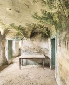 an old room with a table and two doors leading to another room that has a mural on the ceiling