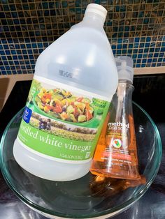 a bottle of white vinegar sitting on top of a glass plate next to an orange liquid