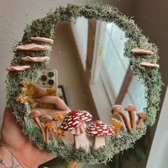 a hand holding up a mirror with mushrooms and moss growing on the surface in front of it