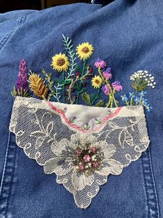 an embroidered piece of clothing with flowers and lace on the bottom, attached to a denim jacket