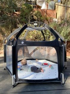 a baby laying on top of a white sheet in a playpen with a black roof