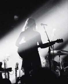 black and white photograph of a person playing guitar in front of microphones on stage