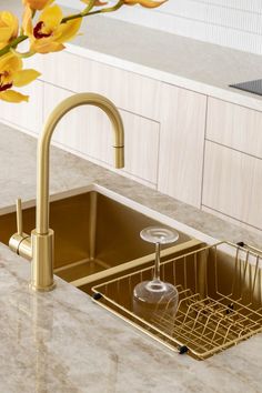 a kitchen sink with a gold faucet next to it and yellow flowers on the counter