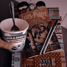 a hand holding a paper cup filled with ice cream next to harry potter books and pencils