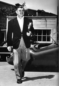 black and white photograph of man walking next to an old car