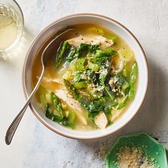 a bowl of chicken and vegetable soup next to a spoon on a white counter top