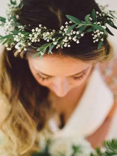 a woman wearing a white dress holding a bouquet of flowers and greenery on her head